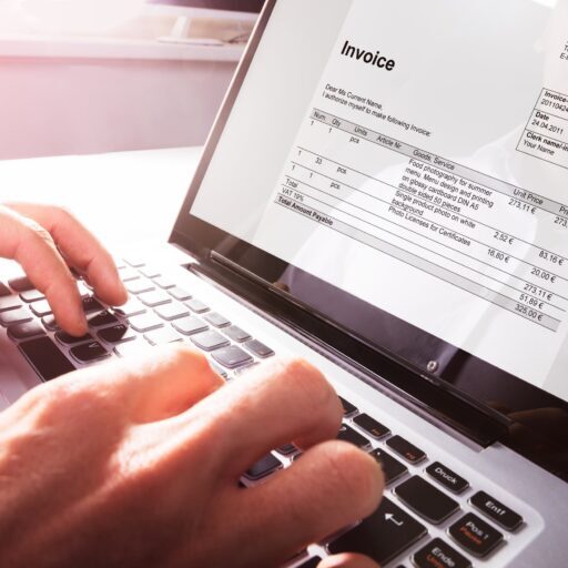 Close-up Of Businessman's Hands Working On Invoice On Laptop At Office